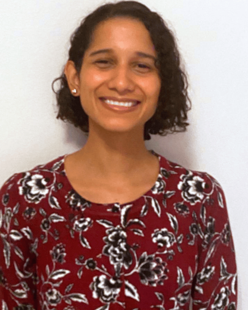 Portrait of a smiling woman with short curly hair wearing a red floral blouse, photographed against a plain background.